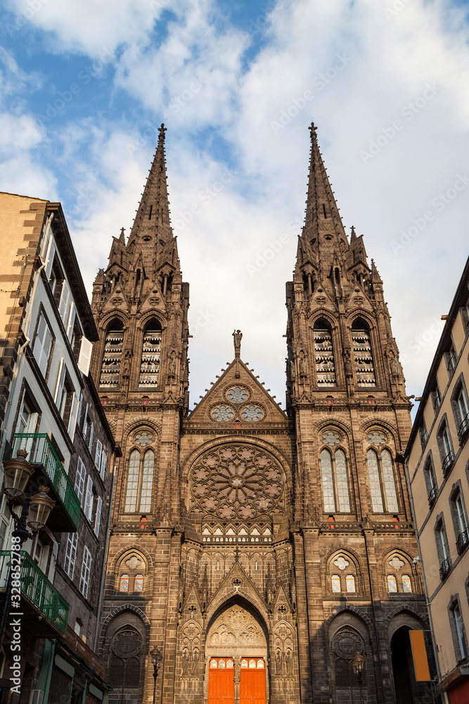 Beautiful, impressive cathedral of Clermont Ferrand in France, made from dark volcanic rocks lighten by golden sunset sun light and old, traditional French buildings
