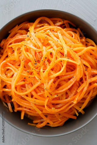 Macro shot of spicy orean carrot salad with oil, garlic and black pepper in grey bowl. Grey table, high resolution photo