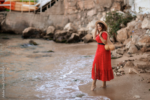 Tourist in red dress walks on wet sand.