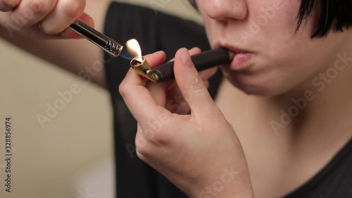 Young girl or teen lighting and smoking brass pipe with medical marijuana weed indoors and exhaling smoke with joy