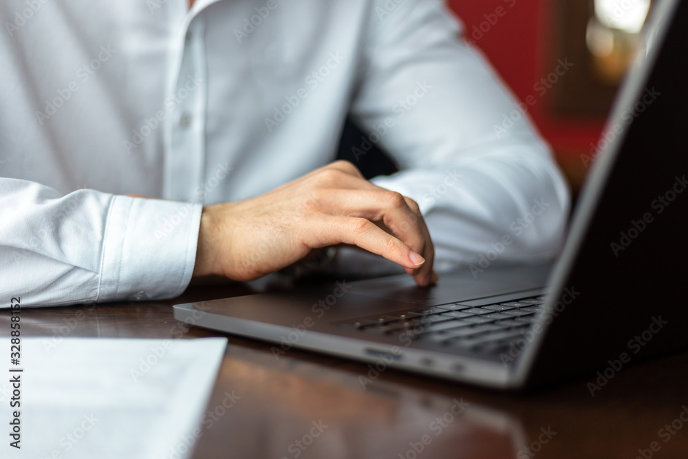 Closeup of hands of young businessman wearing a white fashion shirt in a cafe with a laptop and documents. Freelance and selfemployment concept. Distance job. Closeup of hands of young businessman wearing a white fashion shirt in a cafe with a laptop and documents. Freelance and selfemployment concept. Distance job.