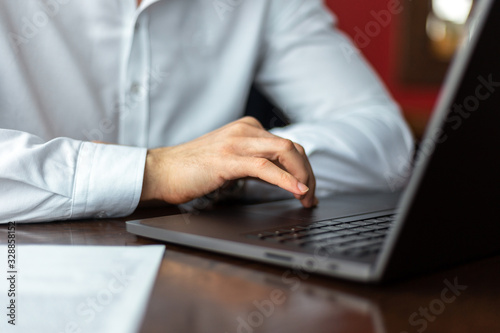 Closeup of hands of young businessman wearing a white fashion shirt in a cafe with a laptop and documents. Freelance and selfemployment concept. Distance job.