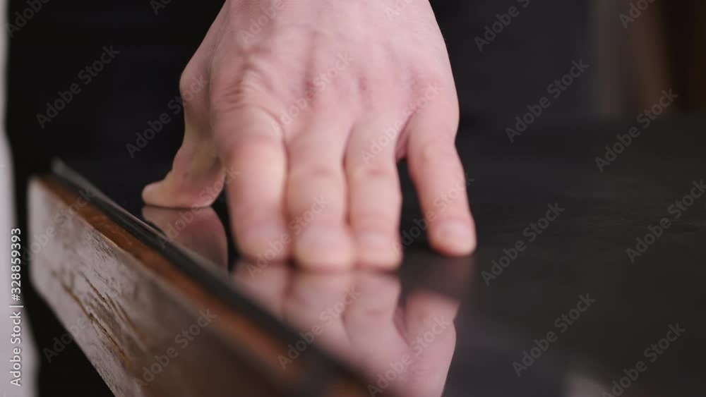 A tanner is cutting black leather sheet with a razor and metre. The master is making a leather belt for men. A tanner is cutting black leather sheet with a razor and metre. The master is making a leather belt for men.