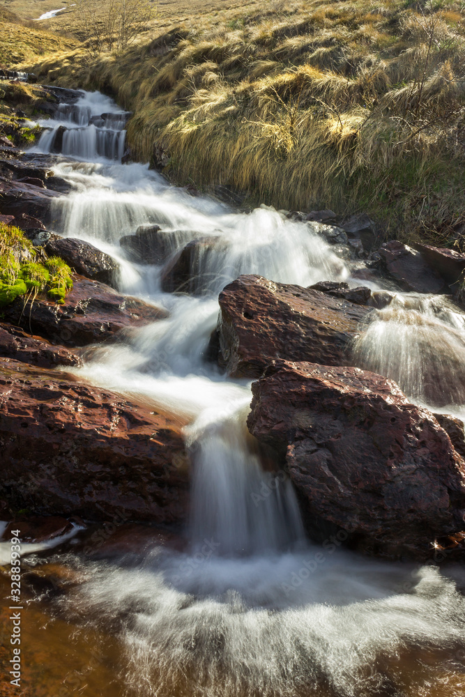 Fototapeta premium Cascades of powerful Monk's jump waterfall, the tallest in Serbia, streaming down the wet, red cliff rocks during early spring