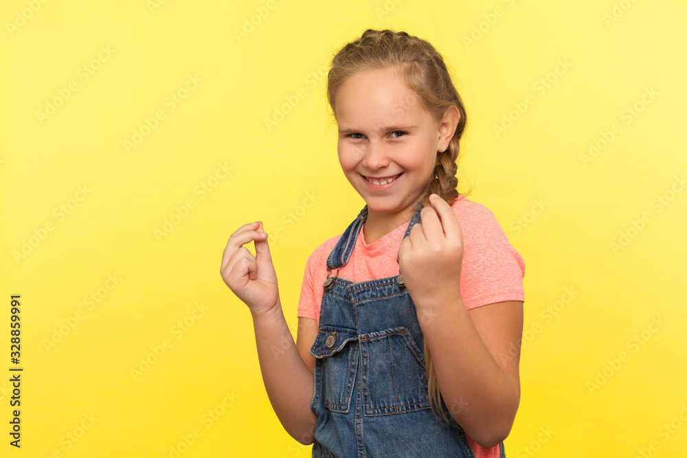 Portrait of funny smiling little girl with braid in denim overalls gesturing i need cash, child demanding pocket money, financial reward, body language. studio shot isolated on yellow background Portrait of funny smiling little girl with braid in denim overalls gesturing i need cash, child demanding pocket money, financial reward, body language. studio shot isolated on yellow background
