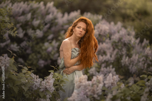 Woman with long red hair on a background of bushes with lilac flowers