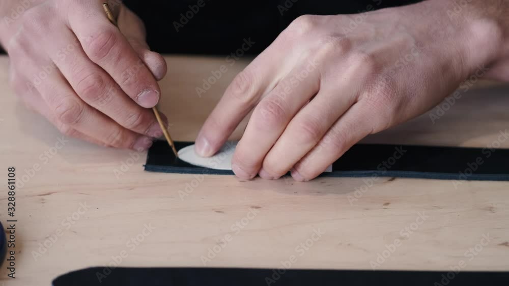 A leather craftsman is marking the end of a belt tail. The tanner is cutting the tail with scissors. A leather craftsman is marking the end of a belt tail. The tanner is cutting the tail with scissors.