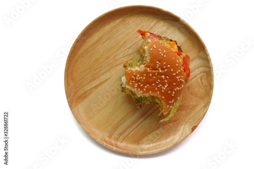 Top view of a partially eaten burger on a round wooden plate, isolated on white background.
