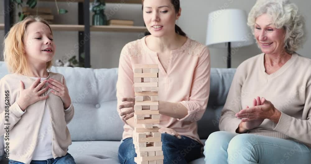 Happy three 3 age generations women family having fun playing jenga board game together. Cheerful young adult mom laughing enjoying funny leisure activity with old grandma and kid grandchild at home.