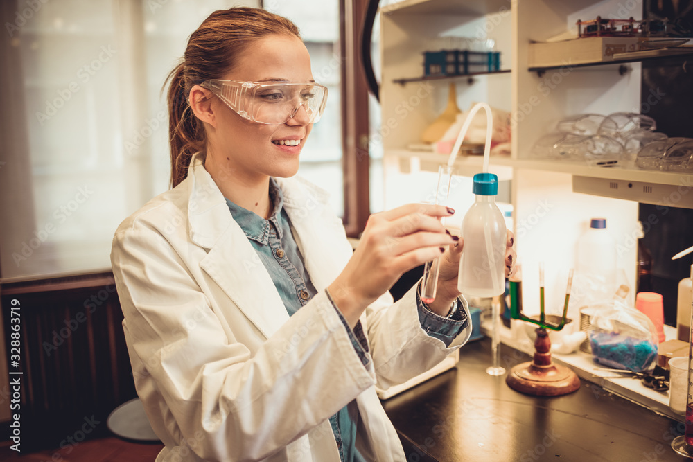 Young attractive female scientist in protective glasses and gloves dropping a liquid substance into the test tube with a long glass pipette in the scientific chemical laboratory Young attractive female scientist in protective glasses and gloves dropping a liquid substance into the test tube with a long glass pipette in the scientific chemical laboratory