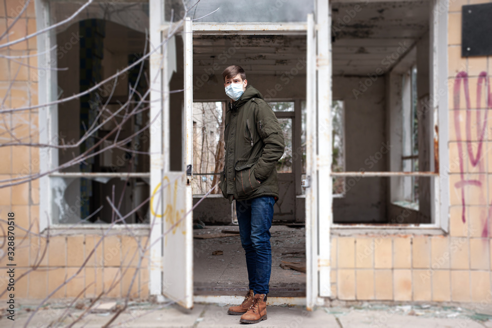 young man in medical mask standing at the entrance to an abandoned hospital building. epidemic shelter young man in medical mask standing at the entrance to an abandoned hospital building. epidemic shelter