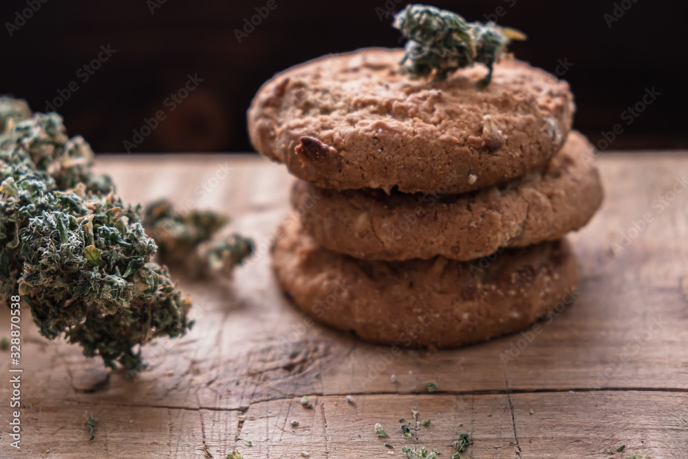 three cookies with marijuana lie on top of each other on a wooden board. Near big bud cannabis. three cookies with marijuana lie on top of each other on a wooden board. Near big bud cannabis.