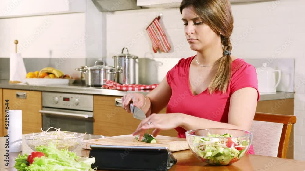 Young woman prepares a salad using a digital tablet to read a recipe on the Internet sitting at a table in the kitchen Young woman prepares a salad using a digital tablet to read a recipe on the Internet sitting at a table in the kitchen