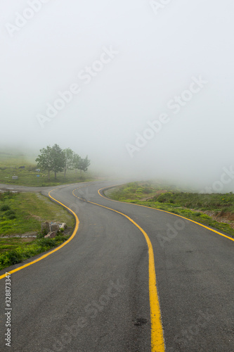 highland road with foggy asphalt yellow lane in spring