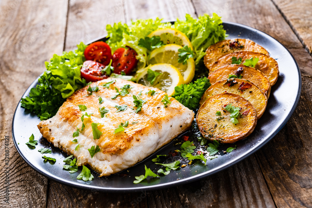 Fish dish - fried cod fillet with potatoes and vegetables on wooden table Fish dish - fried cod fillet with potatoes and vegetables on wooden table