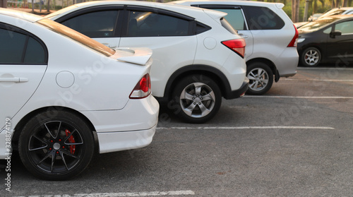 Closeup of rear, back side of white car with other cars parking in outdoor parking area in twilight evening. 