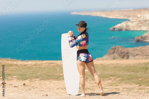 A woman with a muscular figure in a cap and a surfboard in her hands