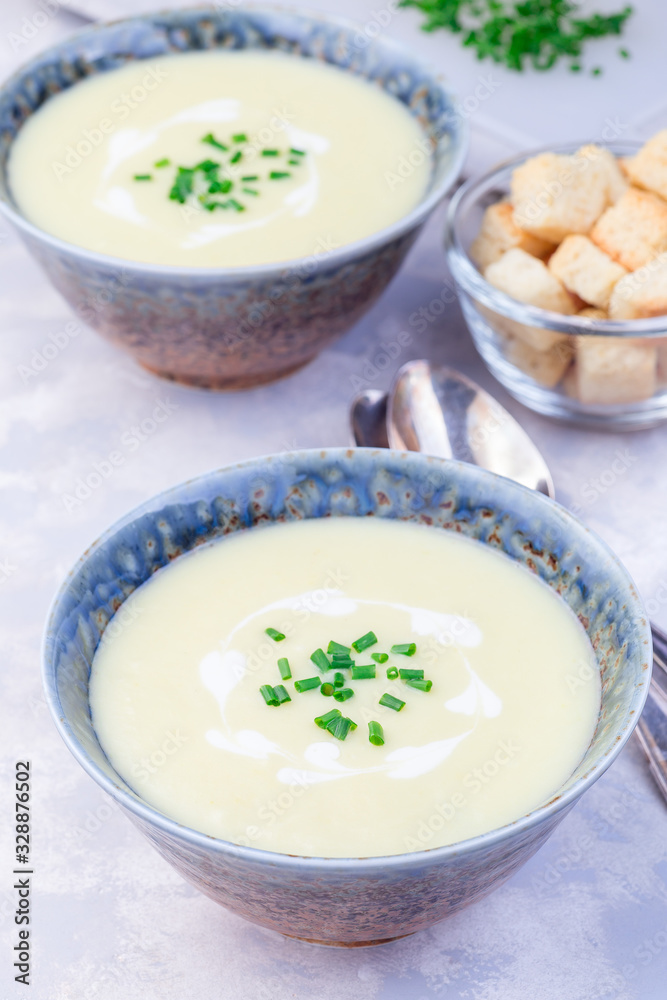 Potato leek soup in blue ceramic bowl garnished with french cream and green onion, vertical Potato leek soup in blue ceramic bowl garnished with french cream and green onion, vertical