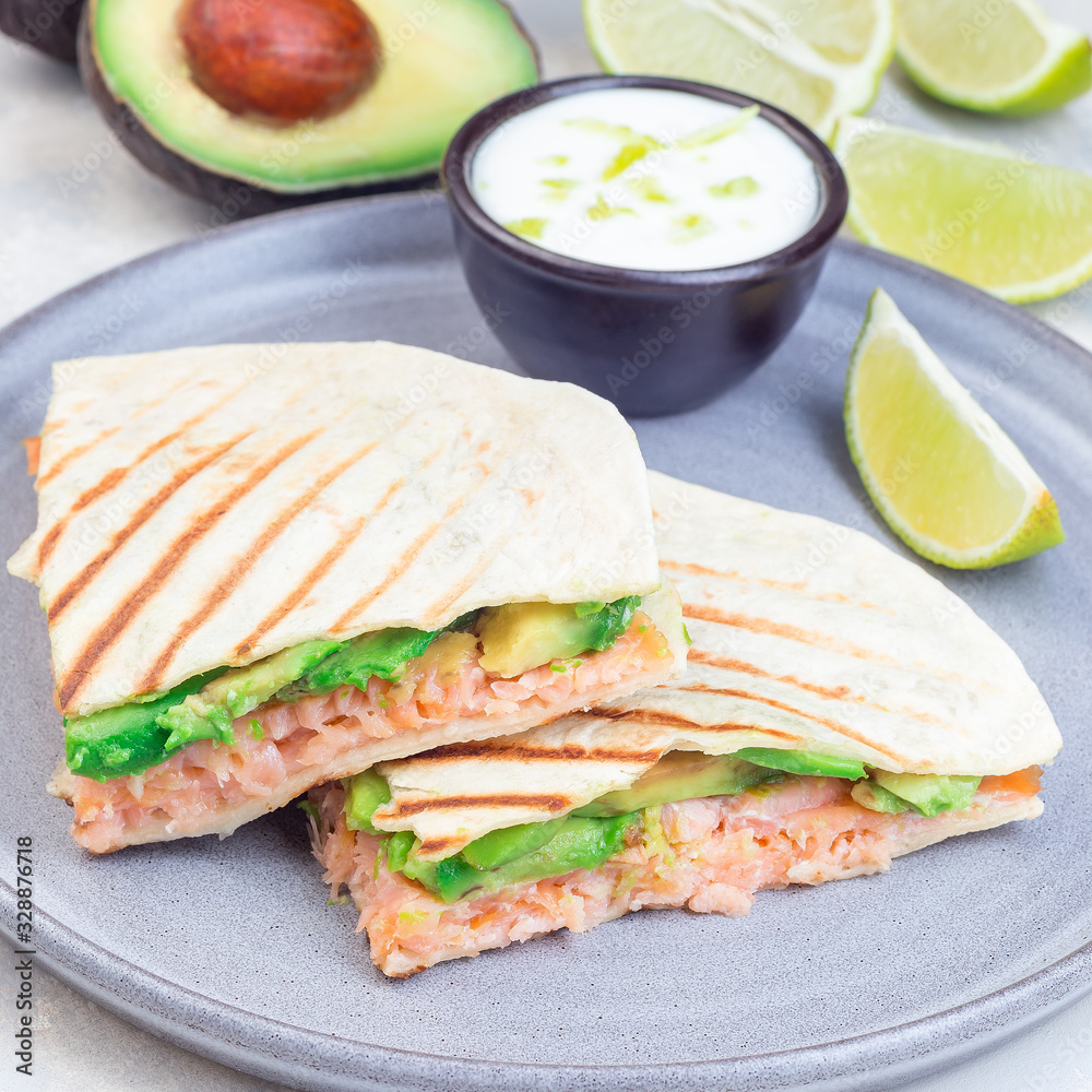Grilled quesadilla with smoked salmon and avocado served with yogurt and lime dip, on gray plate, square format, closeup Grilled quesadilla with smoked salmon and avocado served with yogurt and lime dip, on gray plate, square format, closeup