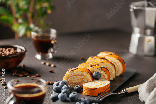 Sweet roll with cream and blueberries on a board on a dark background