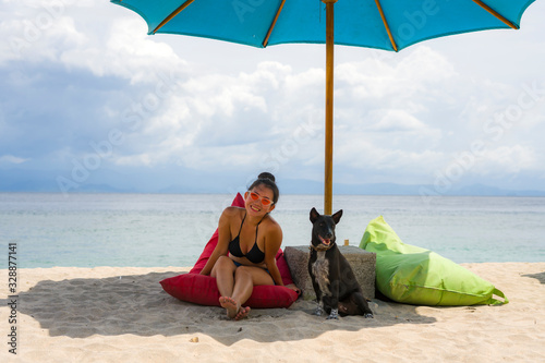 outdoors portrait of young happy and attractive Asian Korean woman in bikini at beautiful beach relaxed and cheerful together with her dog enjoying summer holidays