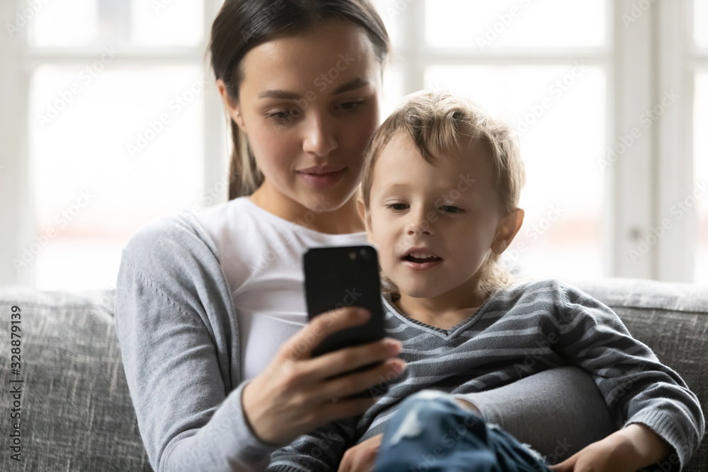 Head shot pleasant young woman cuddling little preschool kid son, taking selfie on telephone. Smiling mommy nanny babysitter showing cartoons or mobile apps to small child boy, resting in living room. Head shot pleasant young woman cuddling little preschool kid son, taking selfie on telephone. Smiling mommy nanny babysitter showing cartoons or mobile apps to small child boy, resting in living room.
