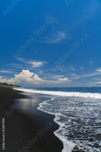 Wave on the black sand of Goa Lawah beach in Bali. The wave rolls on the shore.