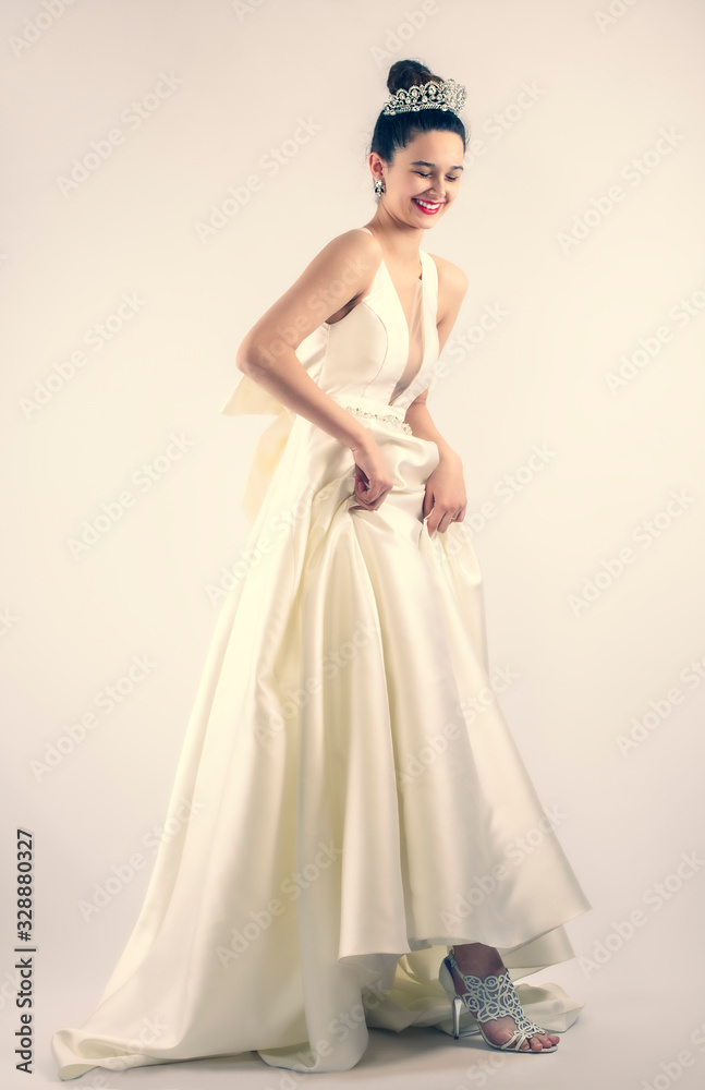 Φωτογραφία cheerful young bride holding the hem of her dress and laughing on gray background