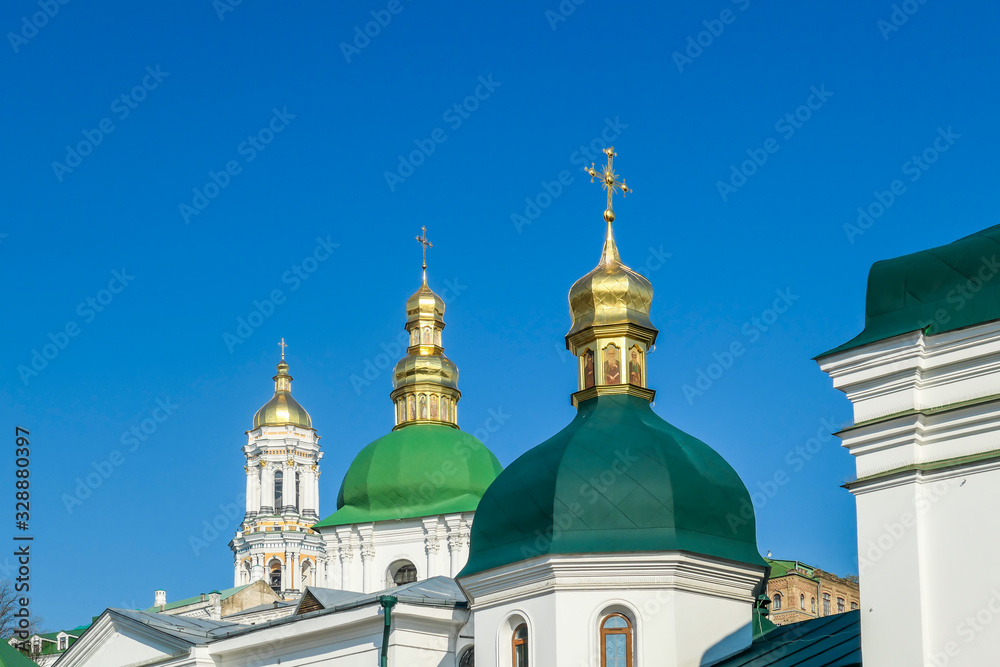 A close-up view on Pechersk Lavra in Kiev, Ukraine, known as the Kiev Monastery of the Caves. Historic Orthodox Christian monastery. Green rooftops with golden domes. Walls are painted white.