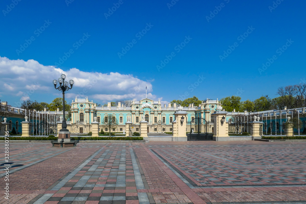Distance view on Mariyinsky Palace, located in Kiev, Ukraine. Palace is painted light blue and sandy colors. Big, open square in front of the palace. Clear and blue sky.