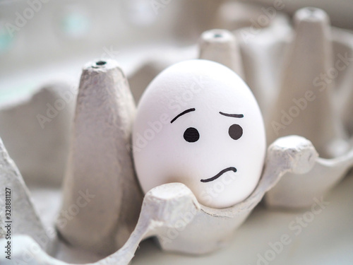 Lonely egg with sad emoji lies in a box