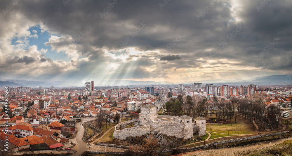 Panorama of beautiful foreground fortress called Momcilov Grad, cityscape of Pirot lighten by amazing sun rays and amazing, colorful, cloudy, sunrise sky 