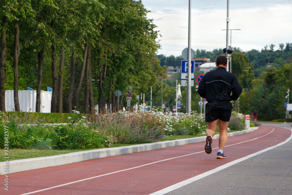 A man in a black suit runs on a red track in a city park. A man in a black suit runs on a red track in a city park.