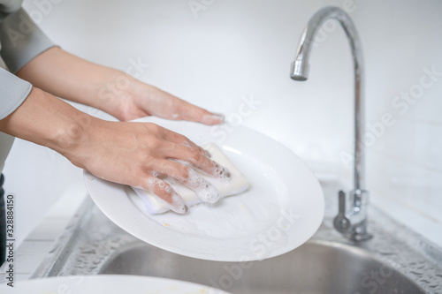 Close up to Asian female washes dish in the kitchen with her dishwashing sponge. photo