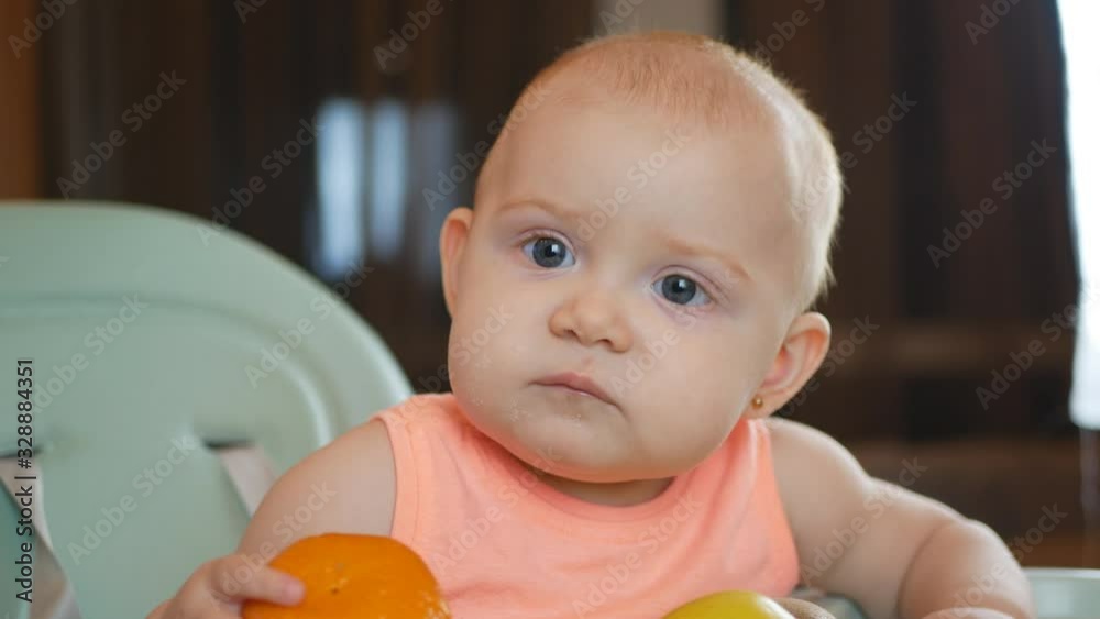 Cute red-haired girl in a high chair tastes fruits. Adorable child tasting fruits. Children's breakfast with fresh fruits. Healthy eating for kids. Toddler enjoying fresh fruits. Healthy eating concep Cute red-haired girl in a high chair tastes fruits. Adorable child tasting fruits. Children's breakfast with fresh fruits. Healthy eating for kids. Toddler enjoying fresh fruits. Healthy eating concep