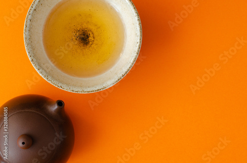 clay teapot and cup of green tea on orange background with copy space. Top view photo