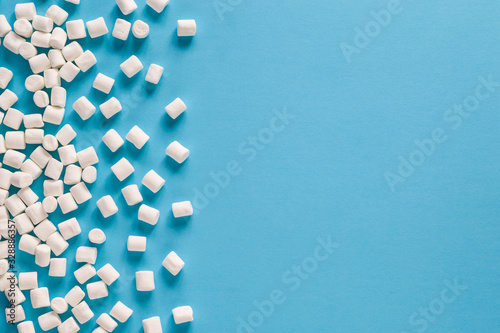 Mini marshmallow on a blue background on the side. White marshmallow frame, background, texture. Copy space, top view.