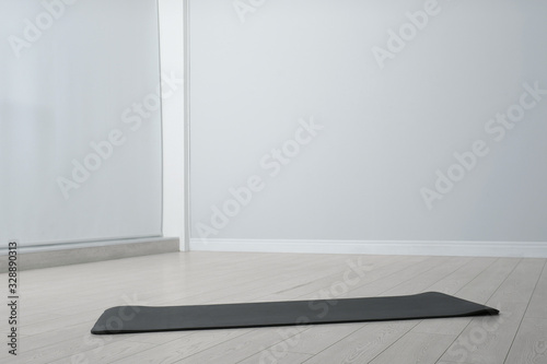 Unrolled black yoga mat on floor in room. Space for text