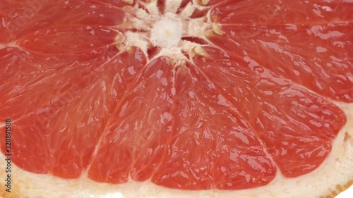 Macro shot of a slice ripe juicy grapefruit being rolled and squeezed. Fresh citrus juice dropping down. Isolated, on white background