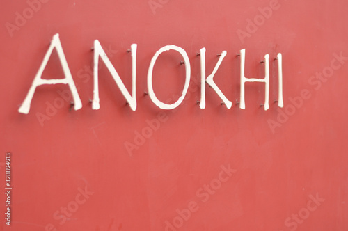 A dark red wall serving as a background with ANOKHI written on it. ANOKHI means UNIQUE in Hindi language