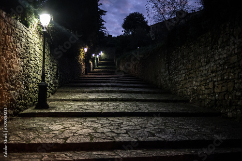 Dark medieval cobbled alley at night with several street lamps providing light