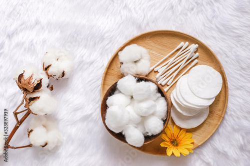 Organic cotton facial pads, cotton balls and cotton buds for removal makeup on wooden tray with natural cotton flowers on white fur background, hygiene and healthy care lifestyle