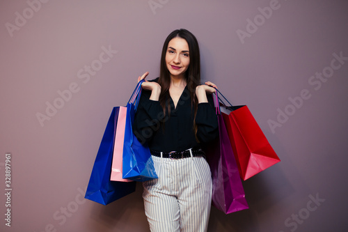 beautiful young woman with colored shopping bags on purple background