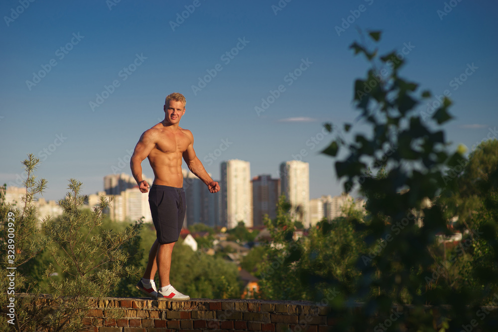 Muscular young man standing on top of the roof and looking at during sunset. Concept of healthy lifestyle and confident 