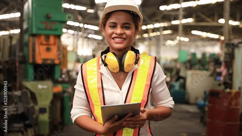 Portrait of professional heavy industry engineer. Technician engineer woman dark skin wearing safety uniform and safety helmet holding digital tablet and smile. Large industrial factory background.