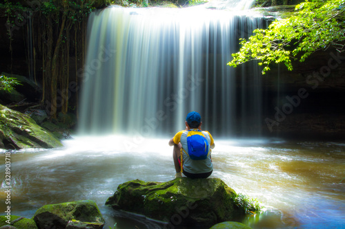 Man sitting on stone front waterfall in forest