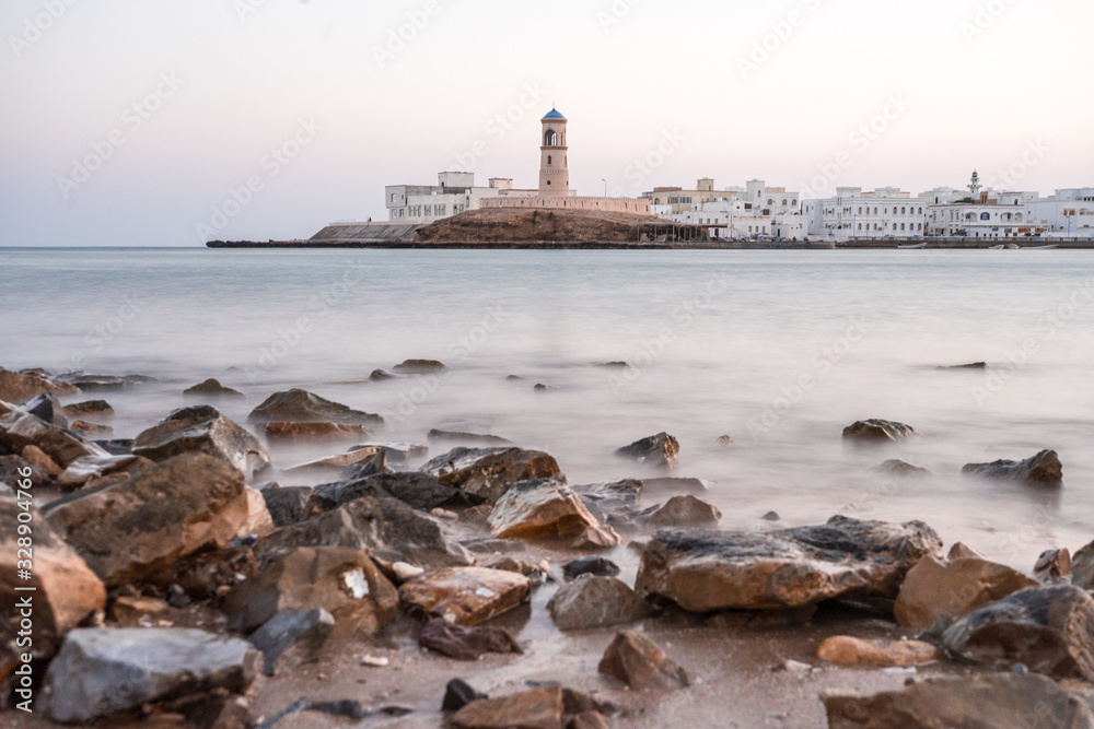 Sunrise on a rocky beach with a lighthouse in the background at Sur's bay, Oman