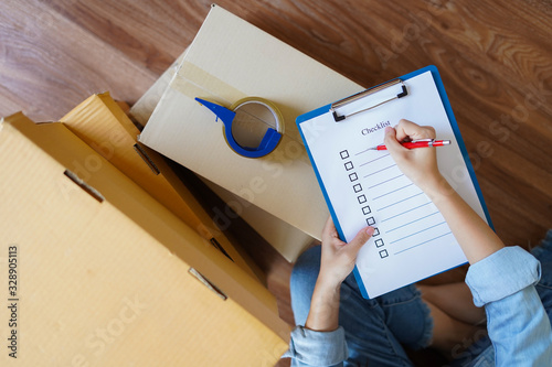 Top view of woman checking package with checklist at home