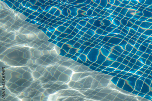 Sun reflection on the blue clear water ripples of swimming pool with mosaic bottom from above.