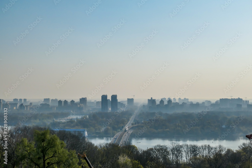 Naklejka premium A panoramic city view on Kiev from a hill. In the middle there is a Dnieper river and a bridge joining two shores of the river. The city is shrouded in fog.